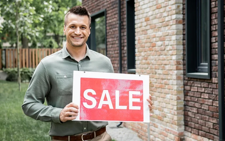 Smiling man holding sale sign in front of property as he uses negative gearing for property investor