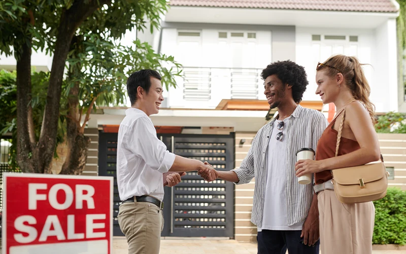 Couple shaking hand of real estate with sold sign in front of investment property